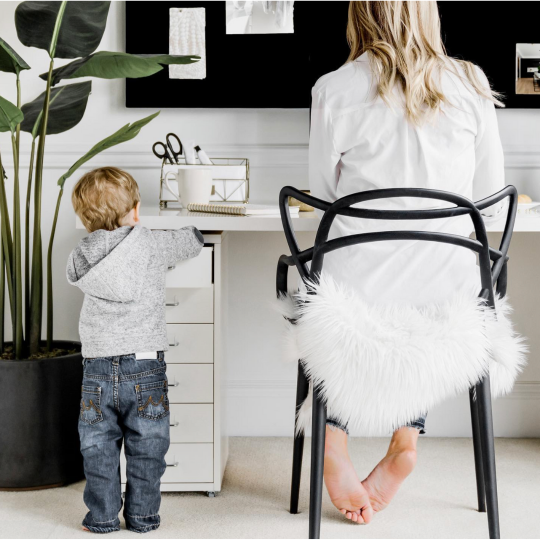 Woman sitting at a desk in a clean, bright, organized, productive workspace at home, along side her child,