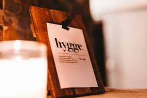 Close-up of a notecard that says hygge on a decorative wooden clipboard with a white candle burning in the foreground creating a warm and cozy vibe